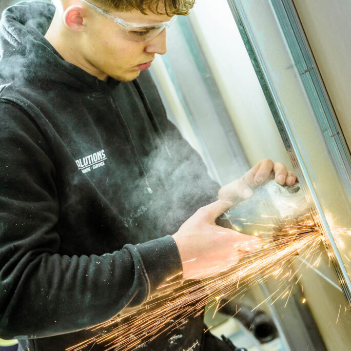 Arbeitende Person mit Winkelschleifer trennt ein Trägerstück in einer Leichtbauwand