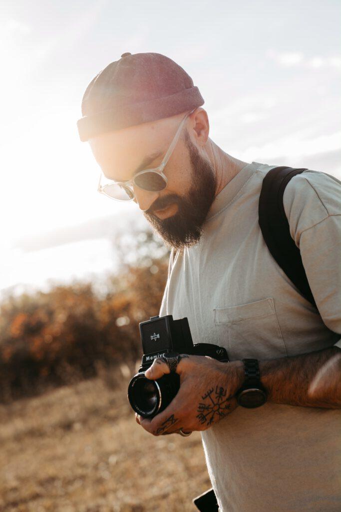 Fotograf Marvin Rust hält eine Mittelformatkamera in Händen, steht im Gegenlicht der Sonne und trägt eine Sonnenbrille