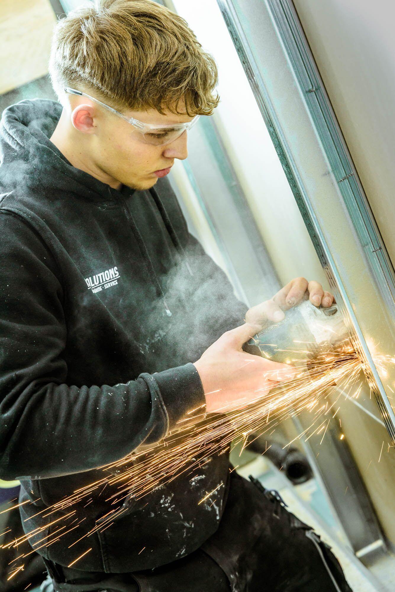 Industriefotografie: Handwerker bearbeitet Metall mit dem Winkelschleifer, Funken fliegen