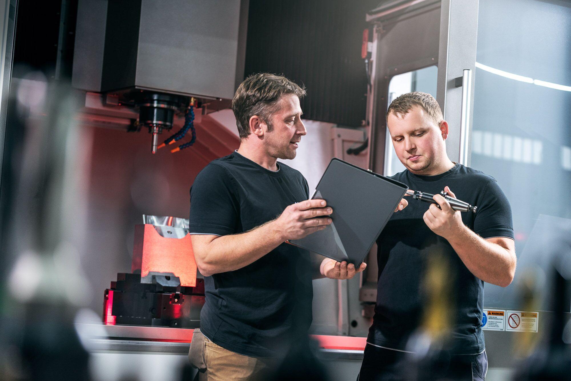 Industriefotografie: zwei Mitarbeiter besprechen an einer Fräsmaschine Daten auf einem Tablet