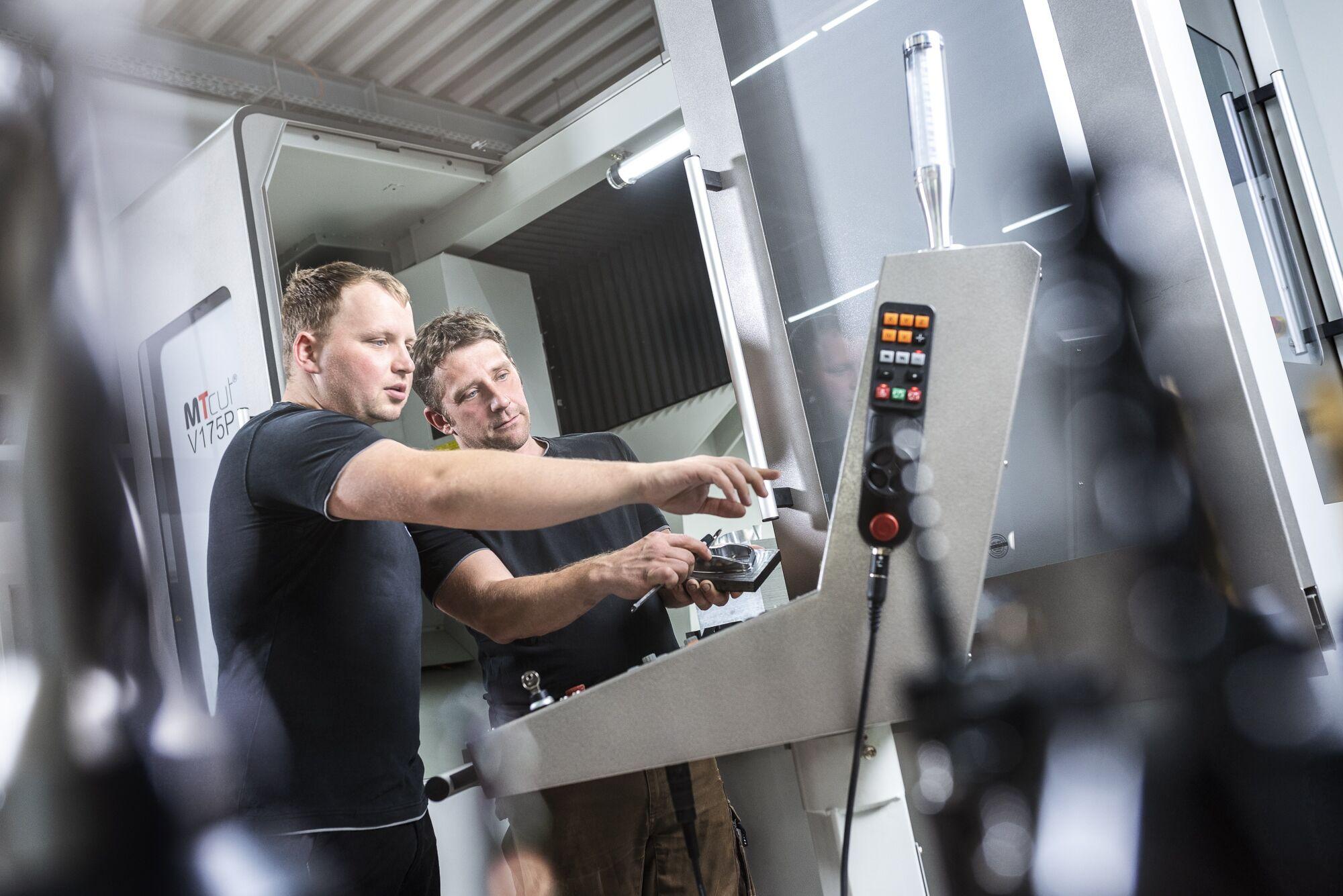 Industriefotografie: zwei Mitarbeiter bedienen gemeinsam das Steuerpult einer CNC-Maschine