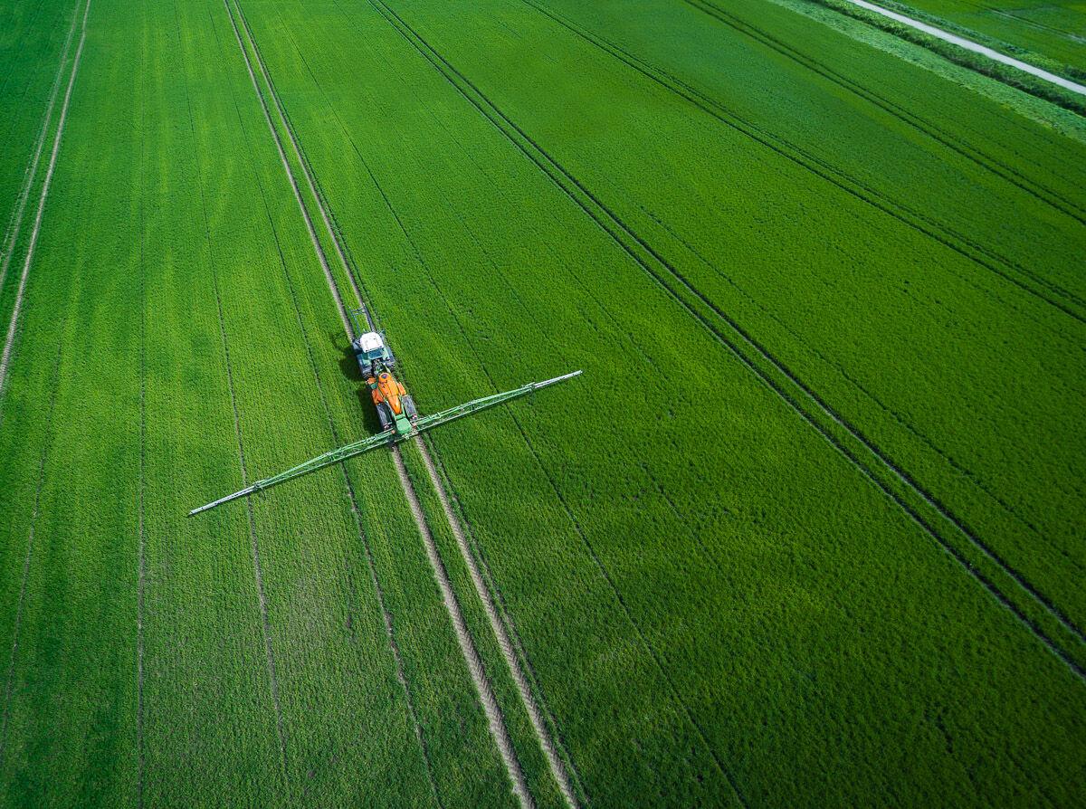Drohnenaufnahme eines Traktors mit Feldspritze auf einem grünen Feld