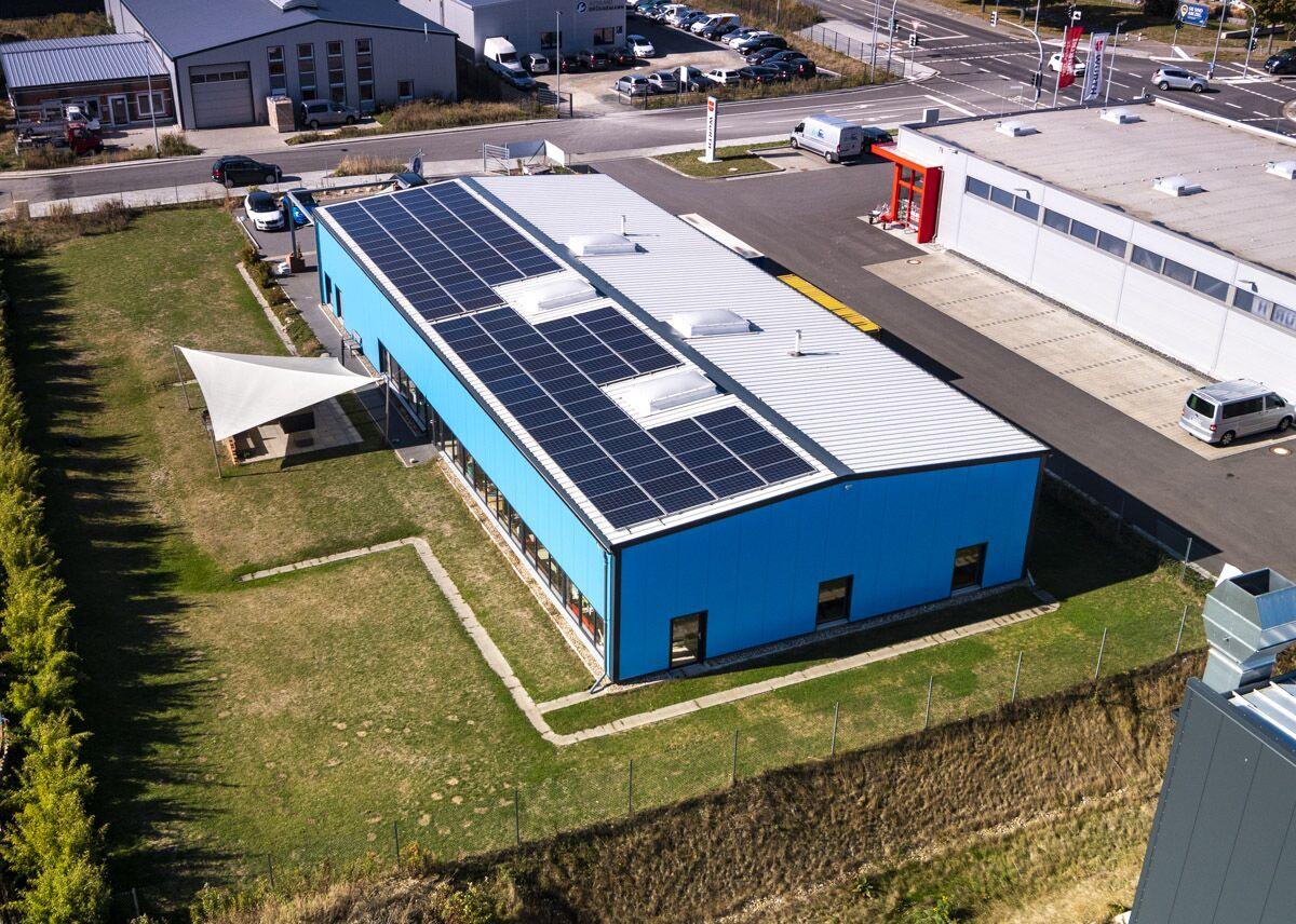 Luftaufnahme per Drohne: blaue Gewerbehalle mit Photovoltaikanlage auf dem Dach