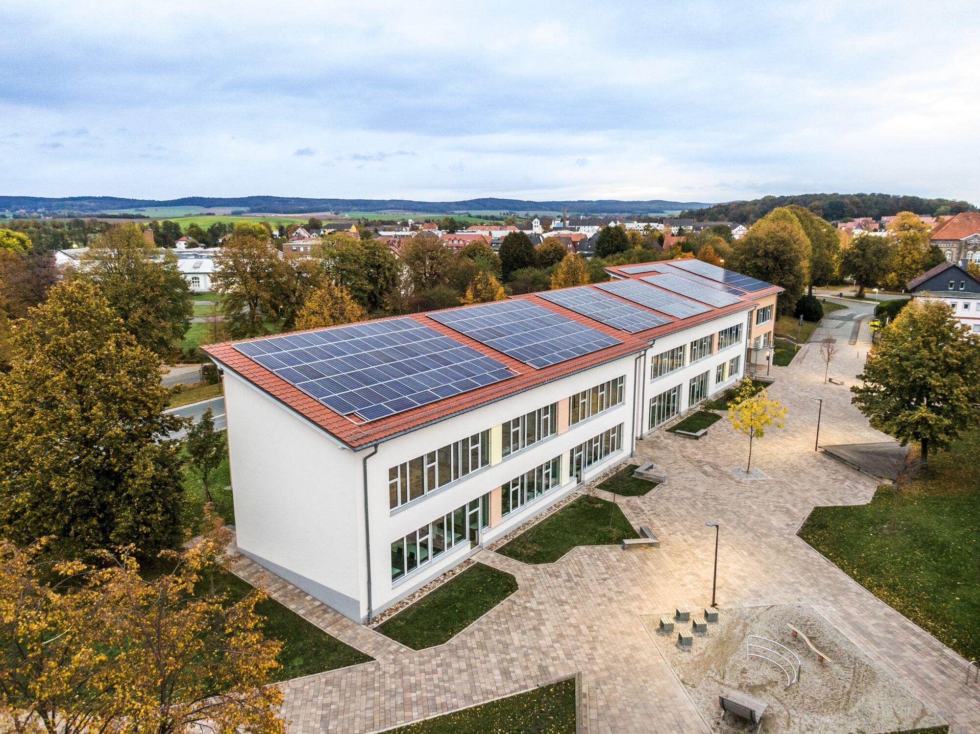 Drohnenfoto eines Schulgebäudes mit Photovoltaik auf dem Dach, umgeben von Herbstbäumen