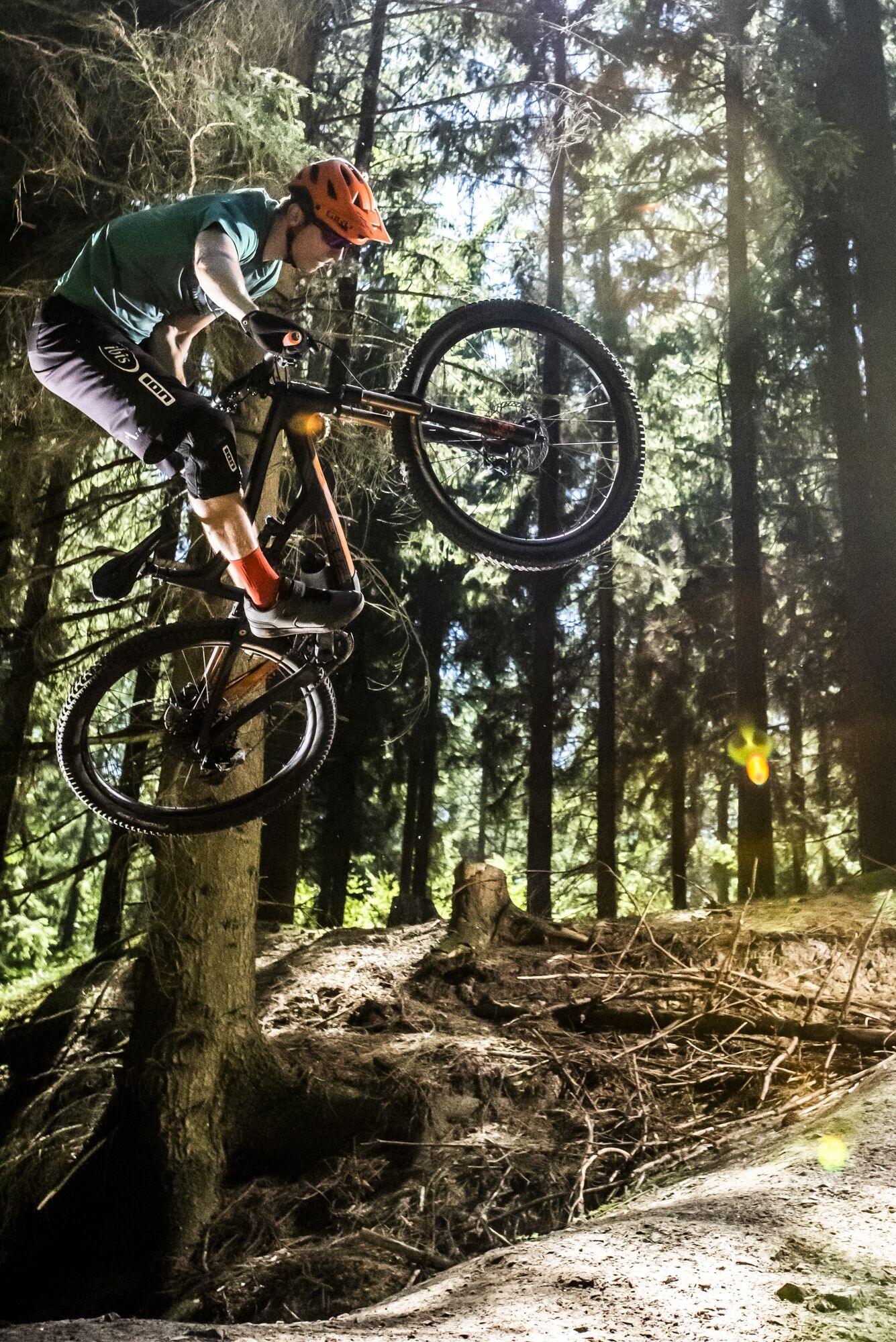 Outdoorfotografie: Mountainbiker springt zwischen Bäumen im Wald