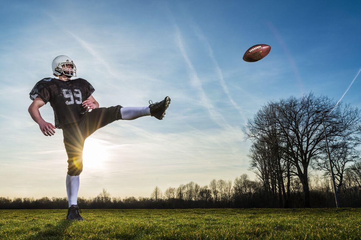 Sportfotografie: American-Football-Spieler beim Kick vor blauem Himmel