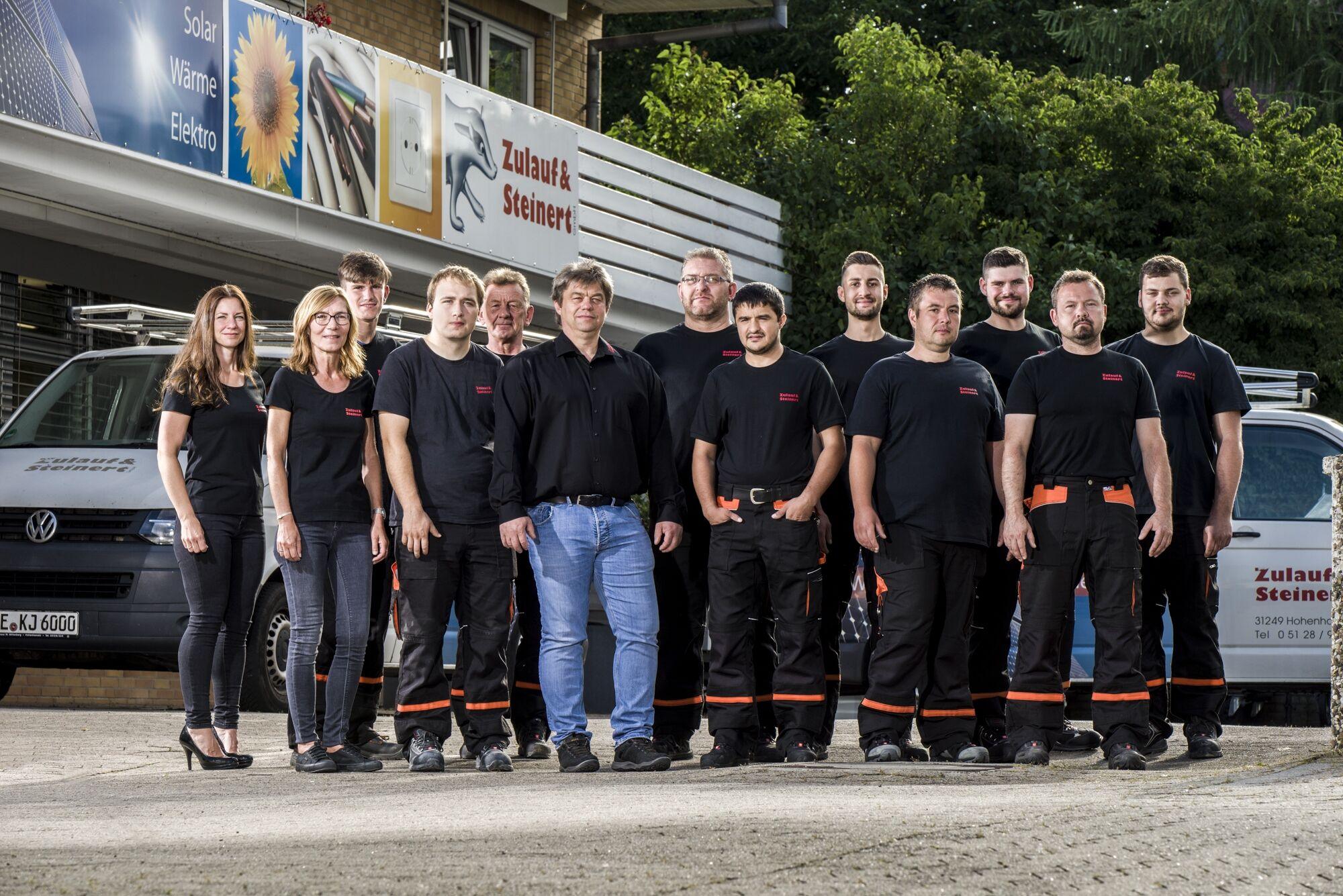 Teamfoto: Belegschaft eines Handwerksbetriebs in Arbeitskleidung vor Firmenfahrzeugen